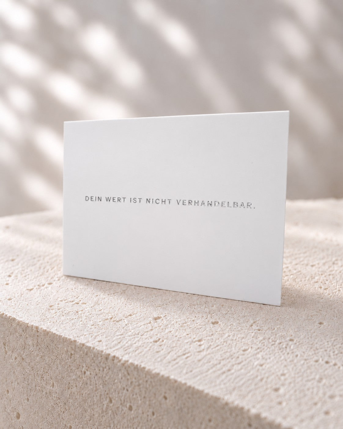 Weiße Edina Jewelry Karte mit silbernem Schriftzug „Dein Wert ist nicht verhandelbar.“ auf hellem Stein.
